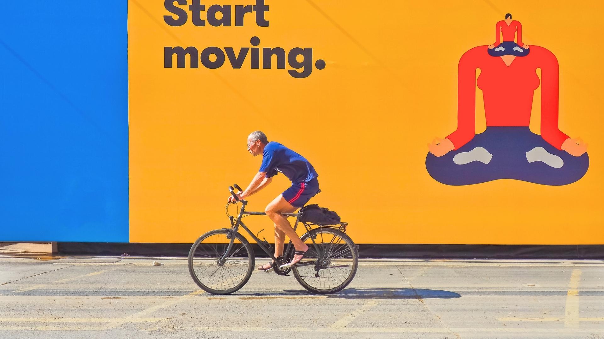 man riding bicycle by yellow and blue wall advertisment