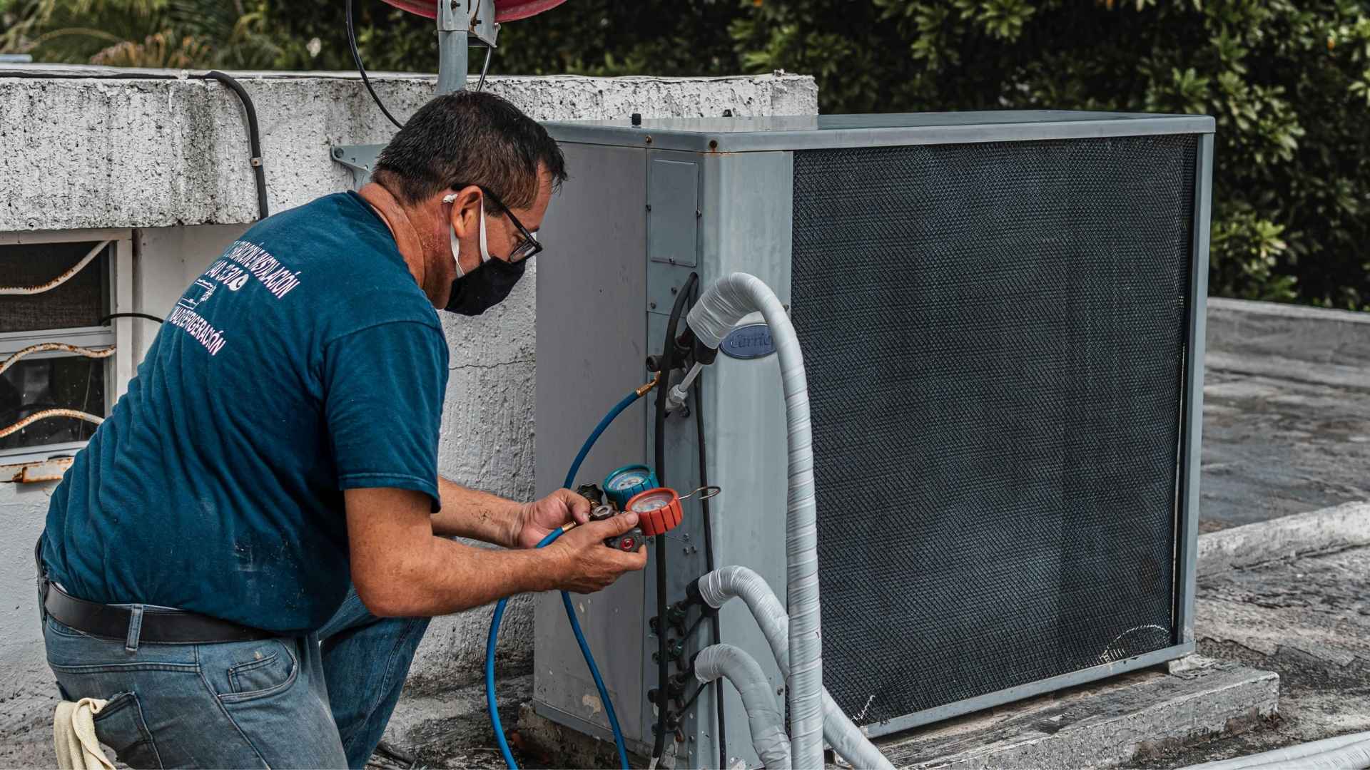 A person in blue clothing is fixing an HVAC system on a roof