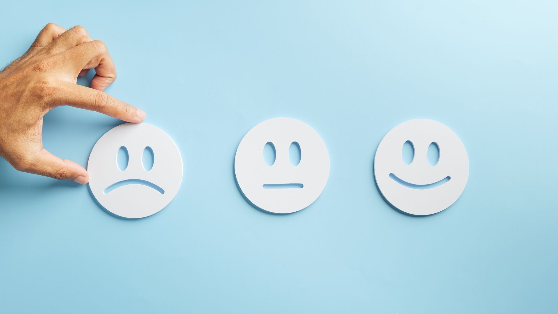 person holding a sad face paper button next to a meh face next to a smile face paper button on a blue backdrop